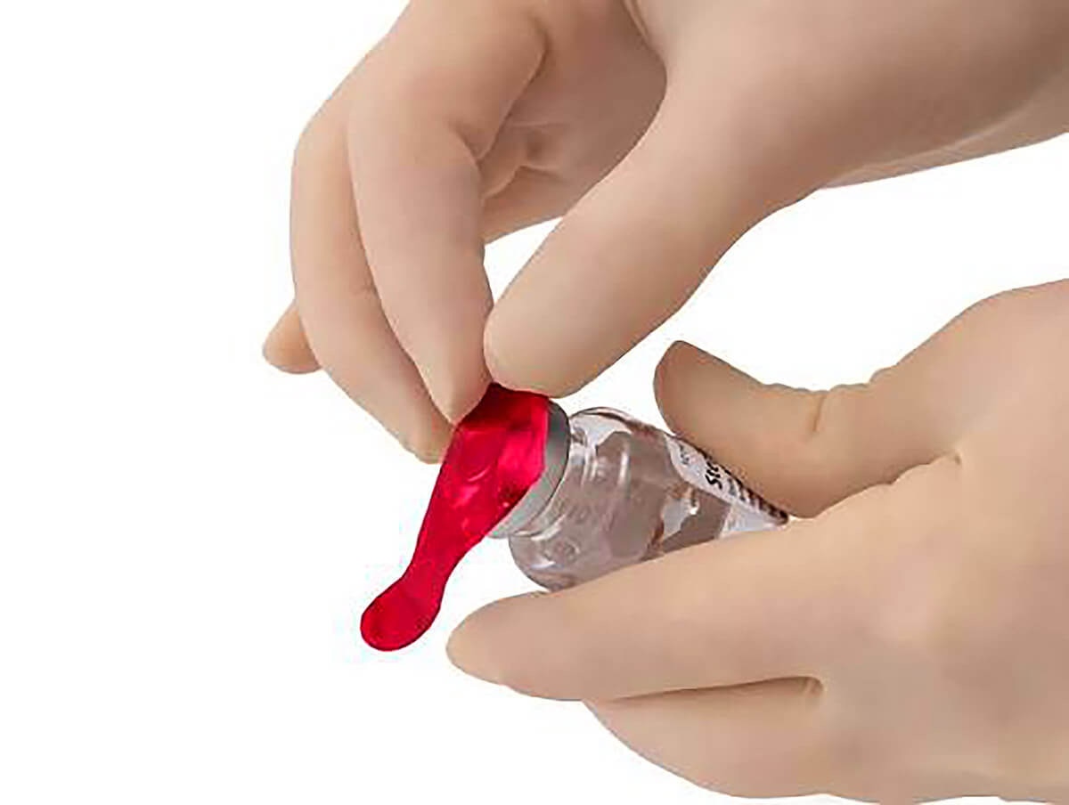 Gloved hands removing a ChemoPlus IVA tamper-evident seal from a medication vial