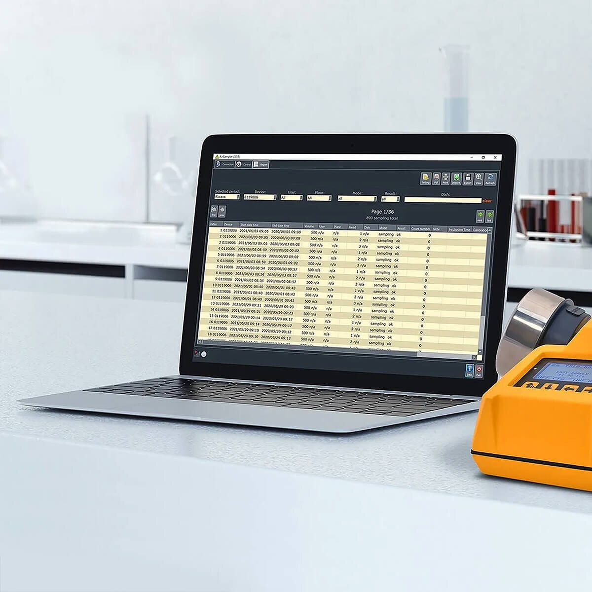 Hardy Diagnostics TRIO.BAS AS Software displaying microbial air-sampling records on a laptop beside a TRIO.BAS air sampler