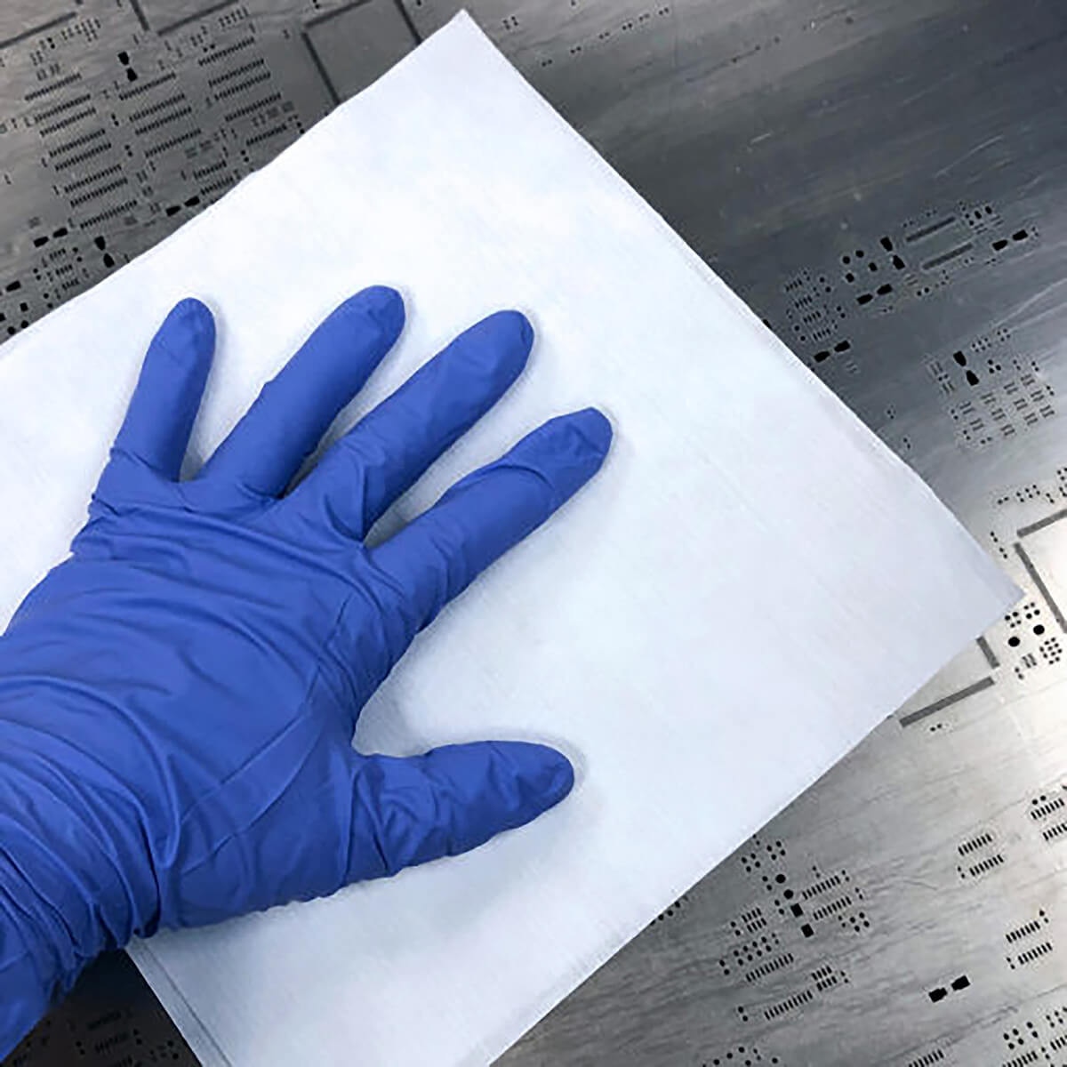 Gloved hand resting on full unfolded AstroWipe sheet on stainless cleanroom surface