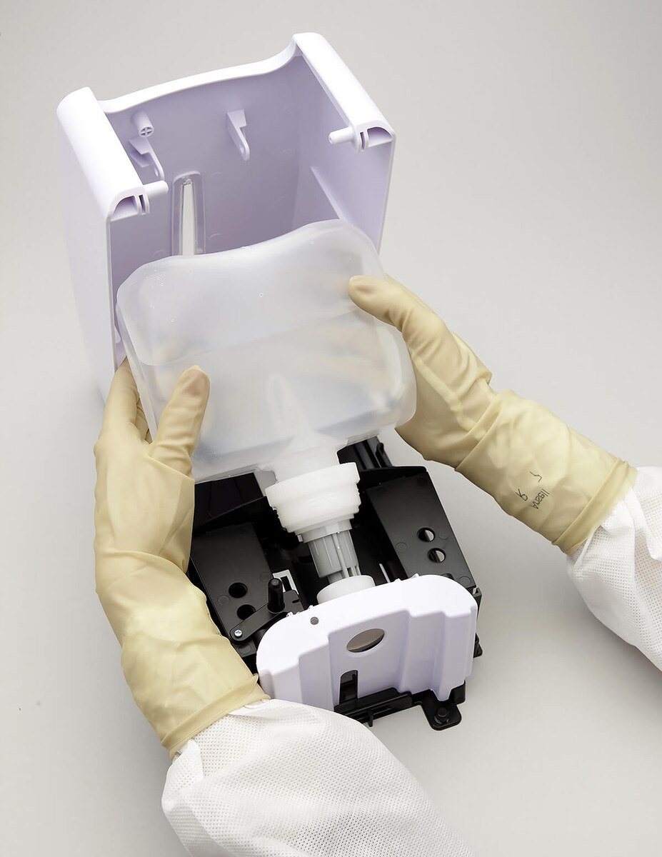 Hands inserting a 32oz refill bottle into an open ASEPTI-CLEANSE dispenser housing, interior components visible.