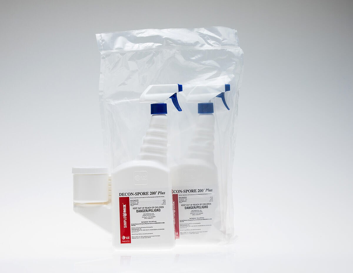 Two DECON-SPORE 200 Plus 5% trigger spray bottles, one standing outside and one packaged in a clear sterile bag behind it, both showing the blue trigger and red label.