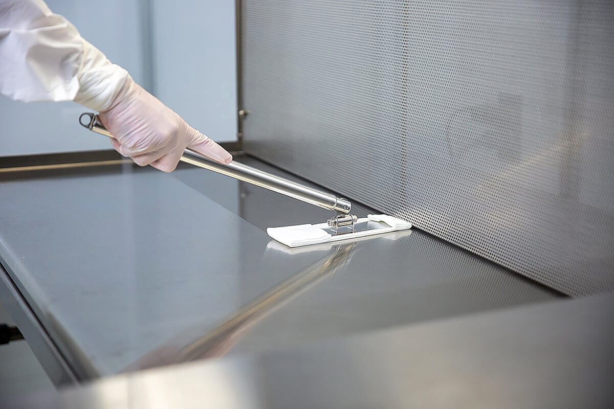 Gloved hand using an EasyReach mop to wipe a metal work surface inside an enclosure.