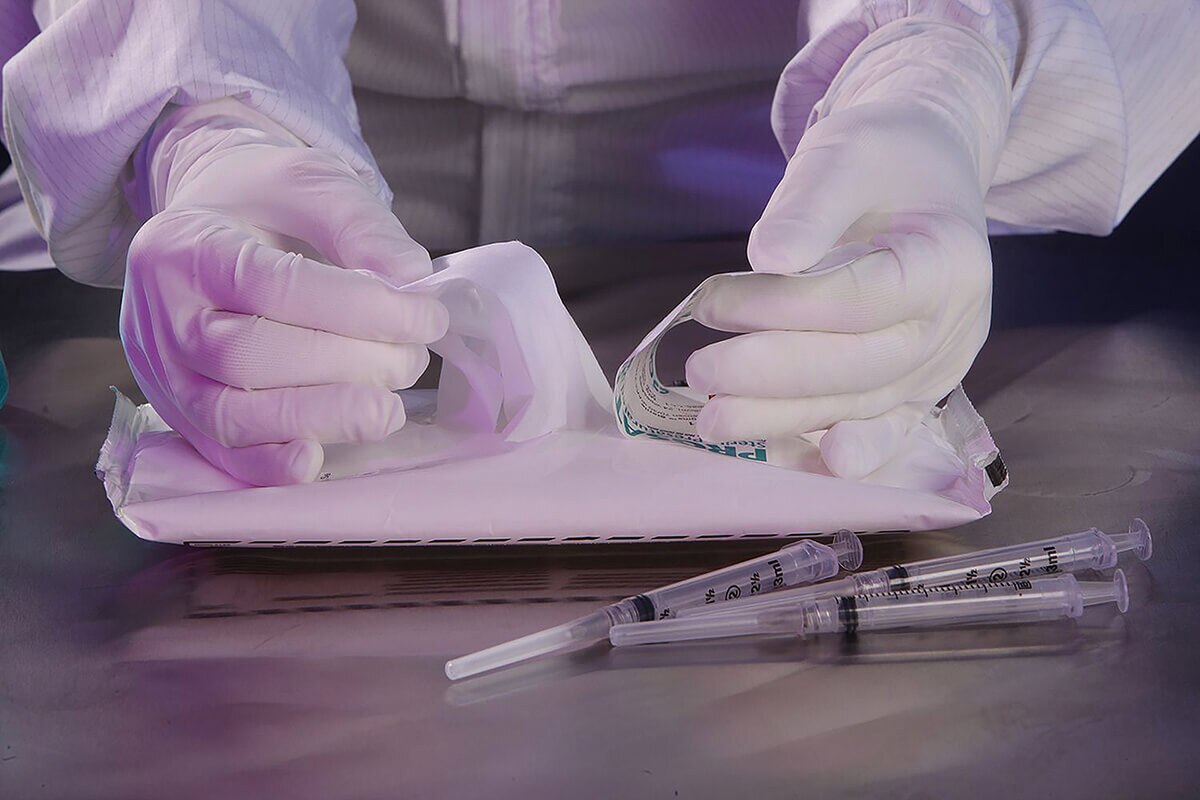 Gloved technician opening a PROSAT Sterile presaturated wipe pouch near syringes inside cleanroom workspace.