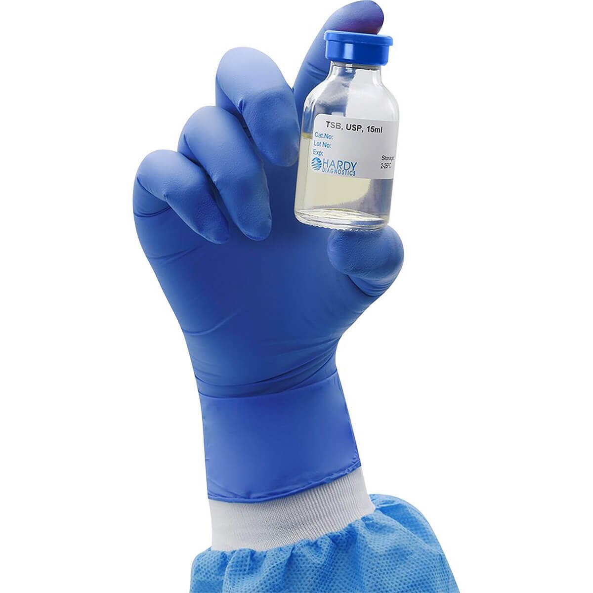 Blue-gloved hand holding a Hardy Diagnostics ReadyRack USP Tryptic Soy Broth glass vial with 15 mL fill and red needle-port septum
