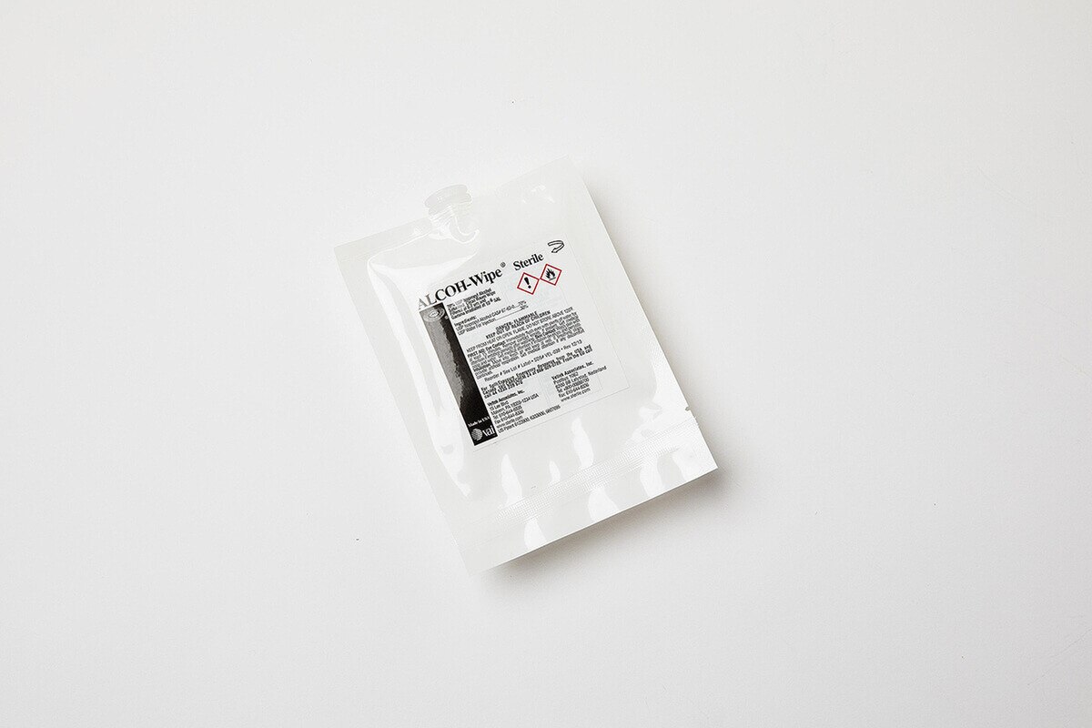 Single sterile pack of ALCOH-Wipe pre-saturated wipes placed on white surface, showing safety icons and product label centered on the pouch
