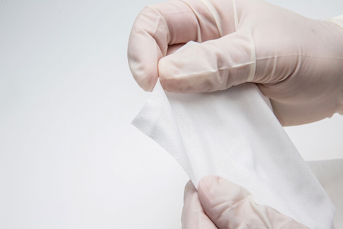 Gloved hands holding and stretching a large sterile textured wipe material showing thickness and durability.